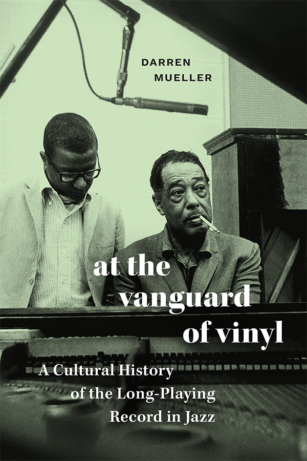 Cover of At the Vanguard of Vinyl: A Cultural History of the Long-Playing Record in Jazz by Darren Mueller. Cover text is in black and white over a photo of Duke Ellington, with a cigarette in his mouth, sitting at a piano. Billy Strayhorn stands next to him, looking down. A microphone hangs over them.